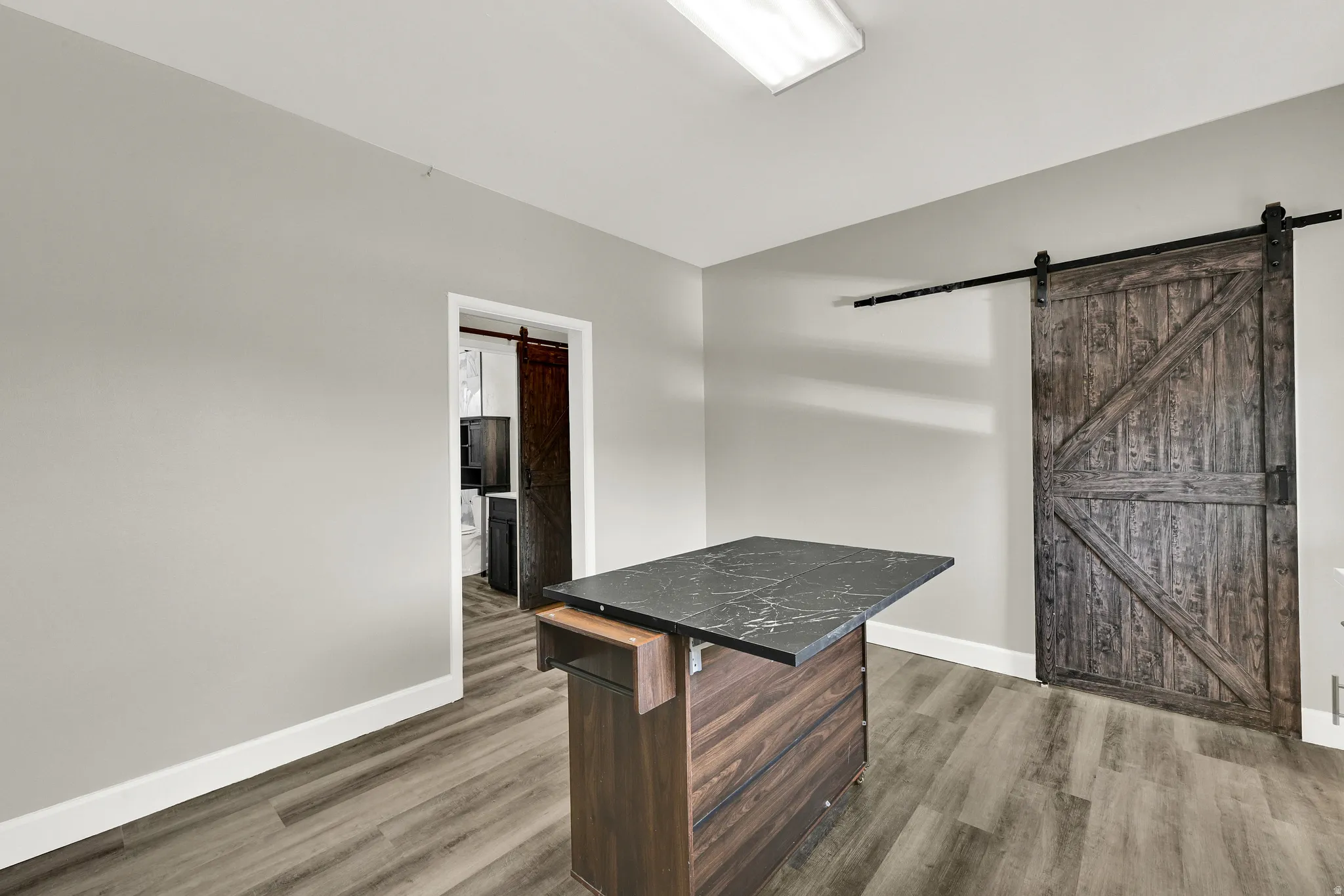 Kitchen island with a dark stone countertop, wood-finish flooring, and a sliding barn door with black hardware