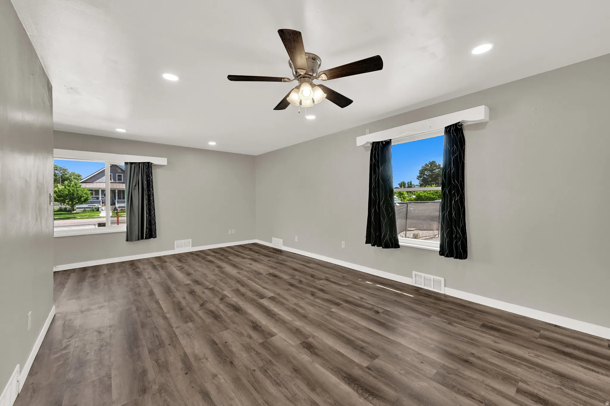 Spacious room featuring wood-finish flooring, light grey walls, recessed ceiling lighting, and a ceiling fan with integrated light fixture
