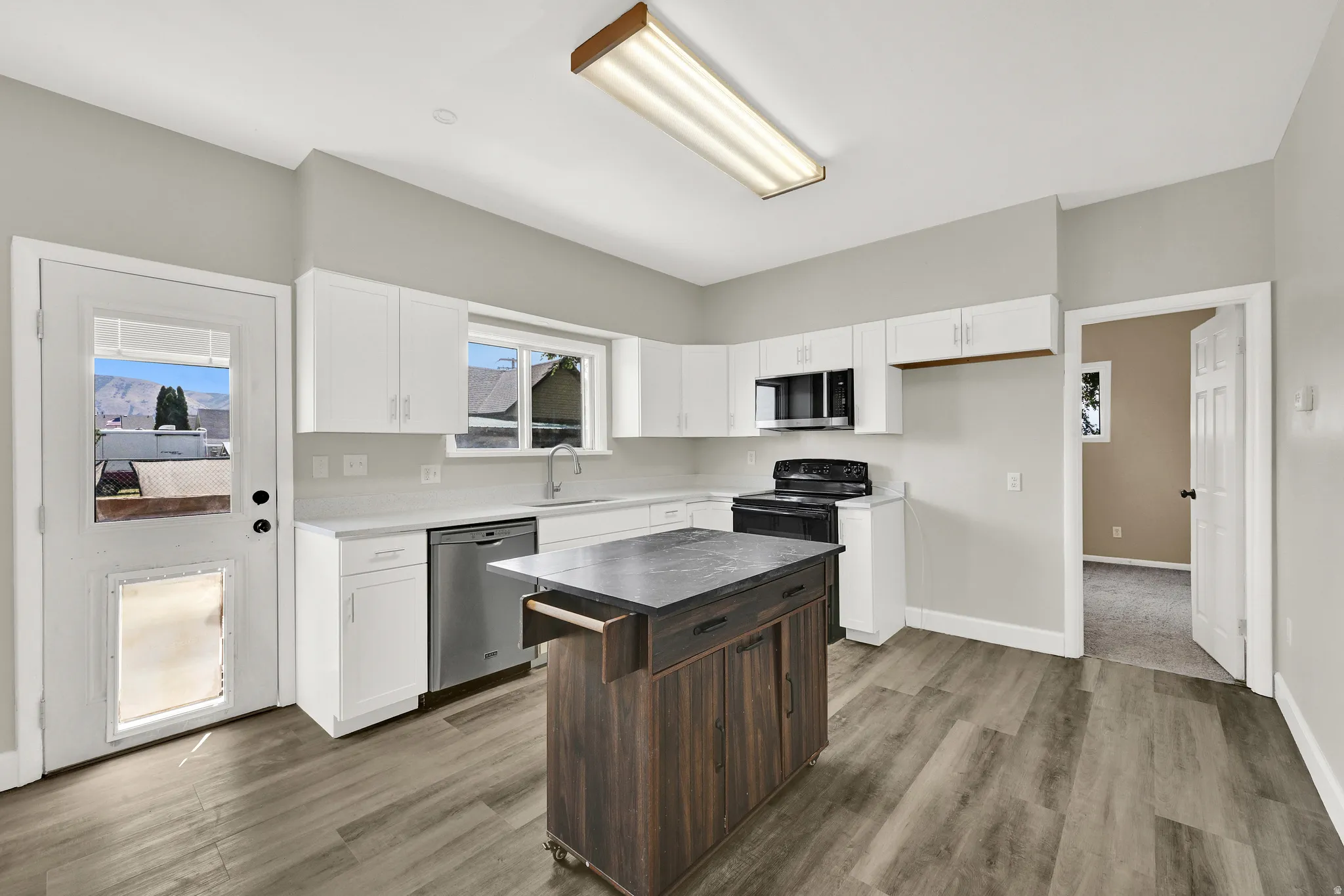 Kitchen featuring wood-finish flooring, white cabinetry, stainless steel dishwasher, black range, and a central island with a contrasting wood-finish base and dark countertop