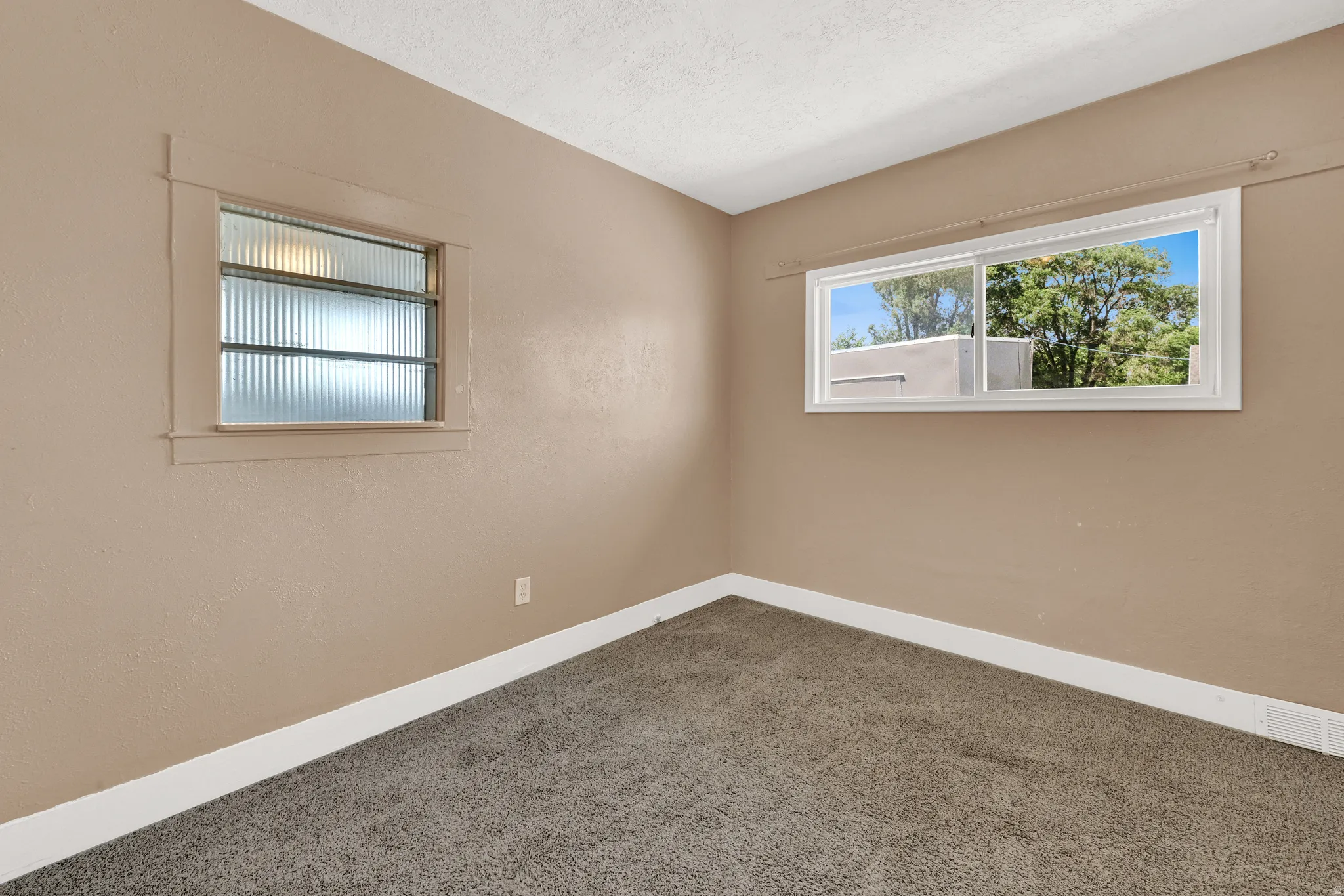 Carpeted room featuring neutral wall tones, white trim, a large sliding window, and a smaller window with textured glass