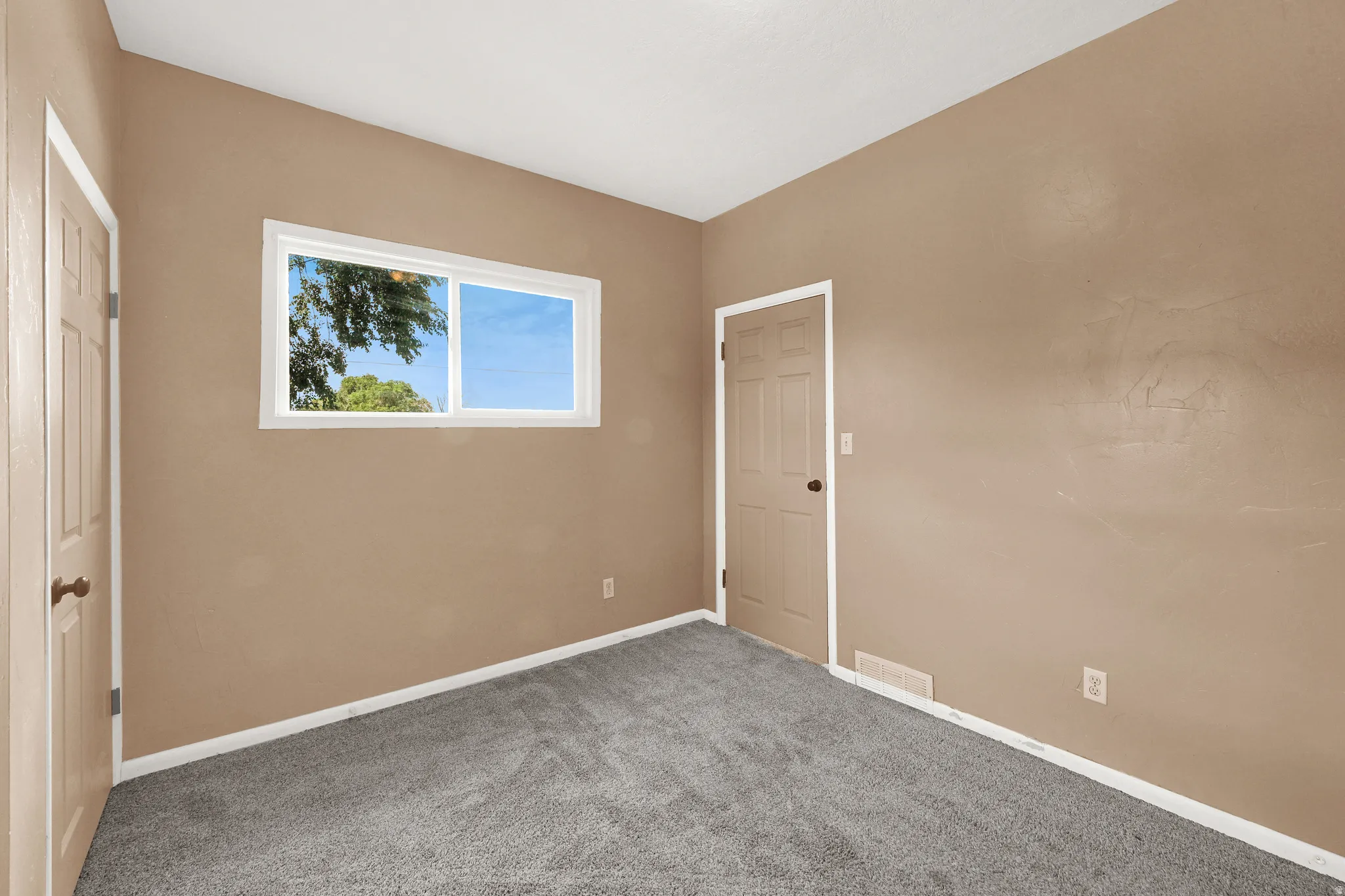 Neutral tone walls with white trim, gray carpet flooring, and a white-framed window