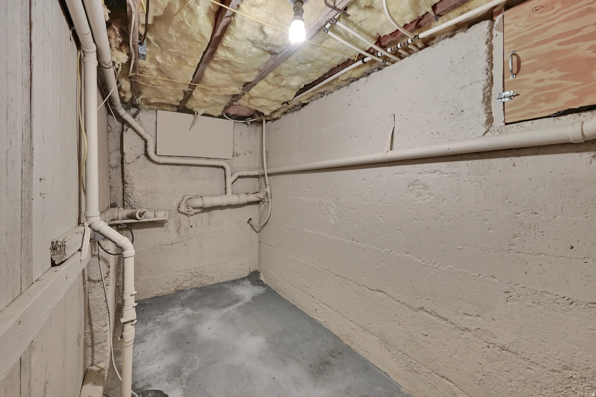 Utility area featuring exposed insulation, overhead piping, and a concrete floor