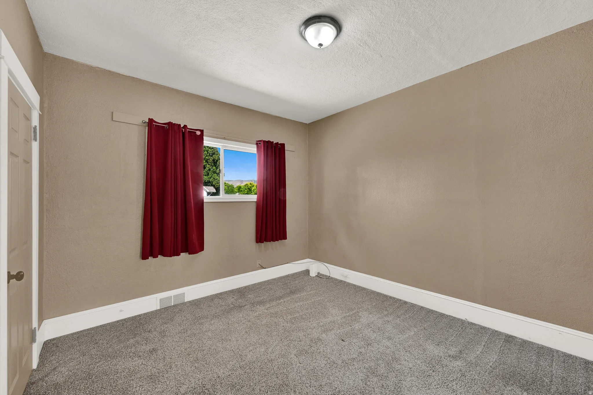 Gray carpeted room with neutral-toned walls, featuring a white trim baseboard