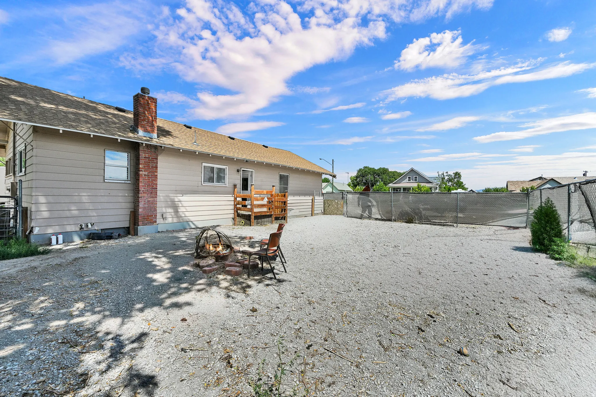 Expansive gravel yard featuring a wood deck, a brick chimney, and perimeter fencing