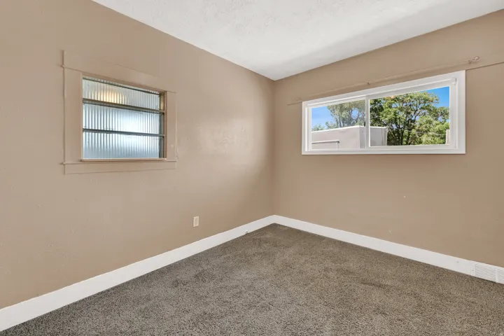 Carpeted room featuring neutral wall tones, white trim, a large sliding window, and a smaller window with textured glass