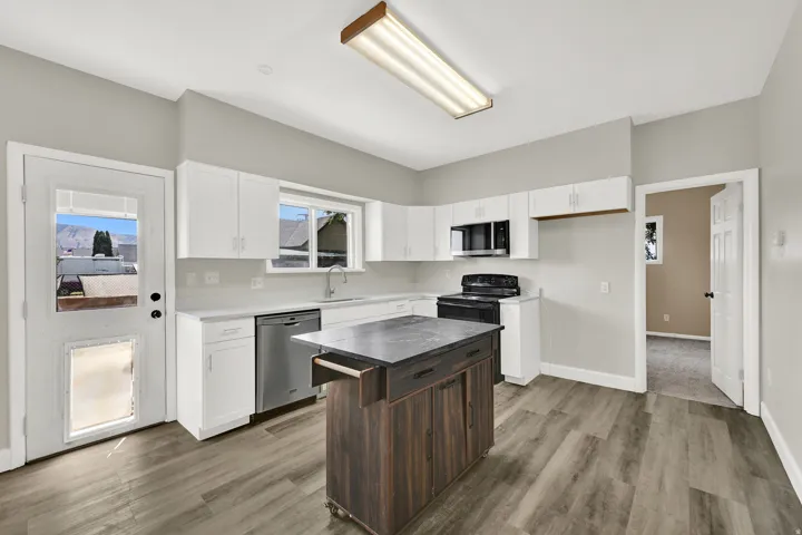 Kitchen featuring wood-finish flooring, white cabinetry, stainless steel dishwasher, black range, and a central island with a contrasting wood-finish base and dark countertop