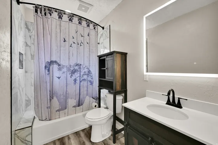 Bathroom featuring a white vanity with an undermount sink, a backlit mirror, and a built-in over-toilet storage cabinet