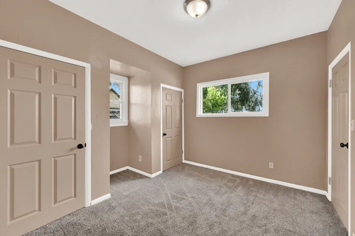 Neutral paint palette room featuring two windows with exterior foliage, gray carpet flooring, and white baseboards