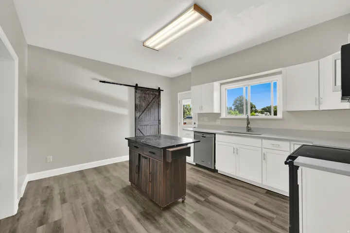 Kitchen featuring white cabinetry, light countertops, stainless steel dishwasher, wood-finish flooring, and a sliding barn door