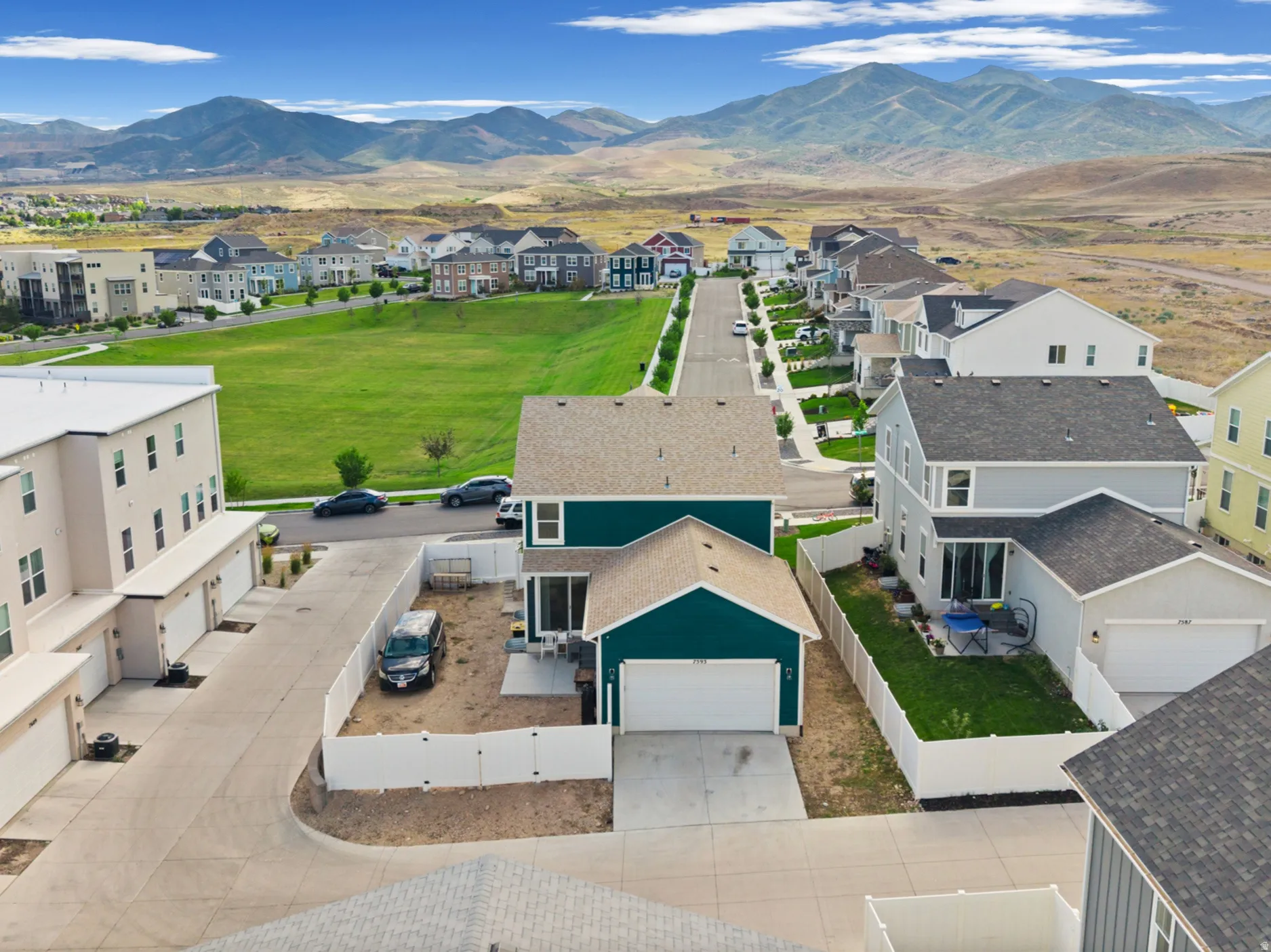 Aerial perspective showcasing a residential street with diverse architectural styles, a verdant open space, and distant mountains