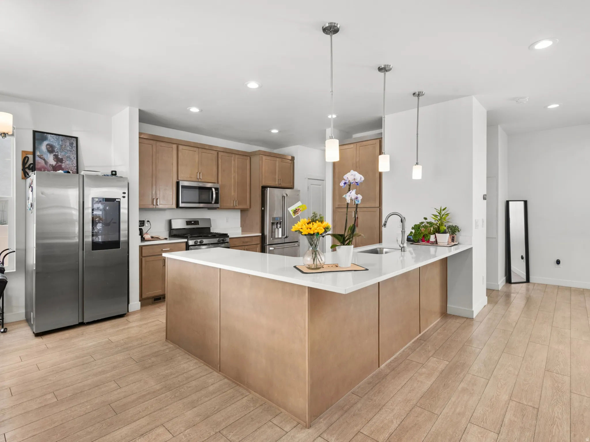 Open-concept kitchen featuring light wood-finish cabinetry, stainless steel appliances, and a central island with a white countertop