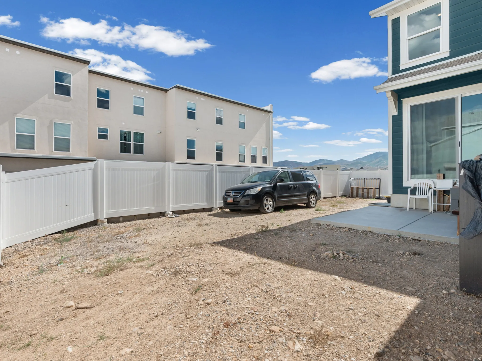 Open outdoor area featuring a white privacy fence, a concrete patio, and a sliding glass door entry to the building