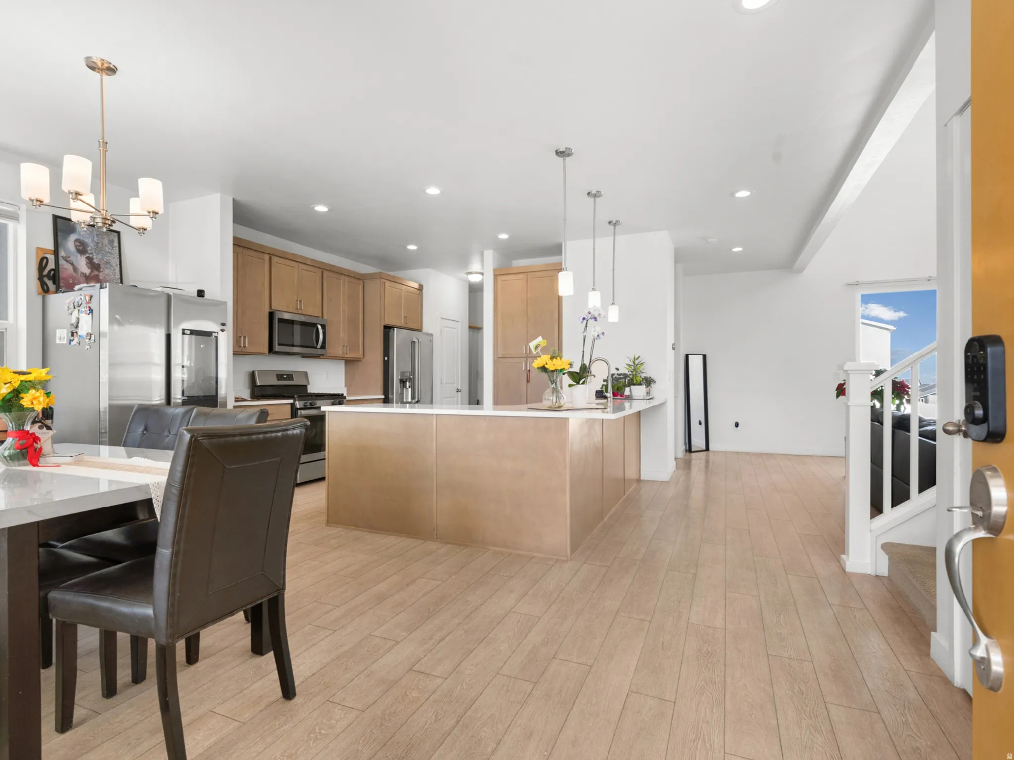 Open-concept kitchen and dining area featuring light wood-finish flooring, a kitchen island with pendant lighting, stainless steel appliances, and wood cabinetry