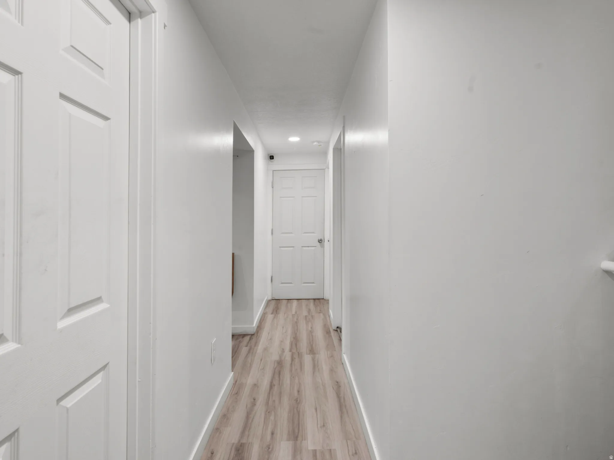 Hallway with wood-finish flooring, white walls, and recessed lighting