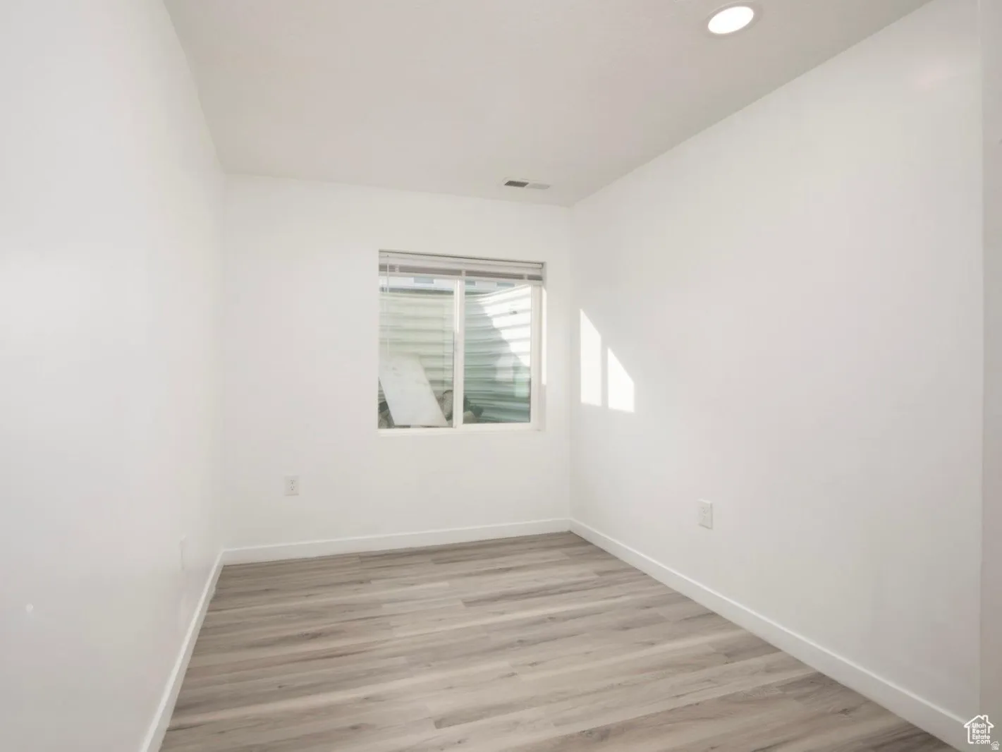 Room featuring light wood-finish flooring, white walls, and a window with blinds