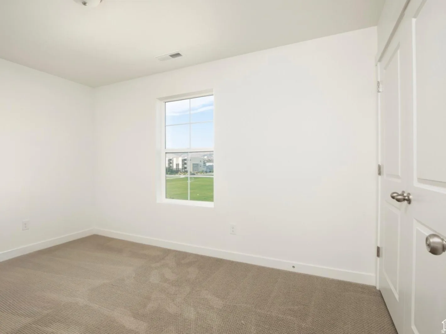 Light-filled interior featuring a single pane window, neutral-toned carpet, white painted walls, and white trim