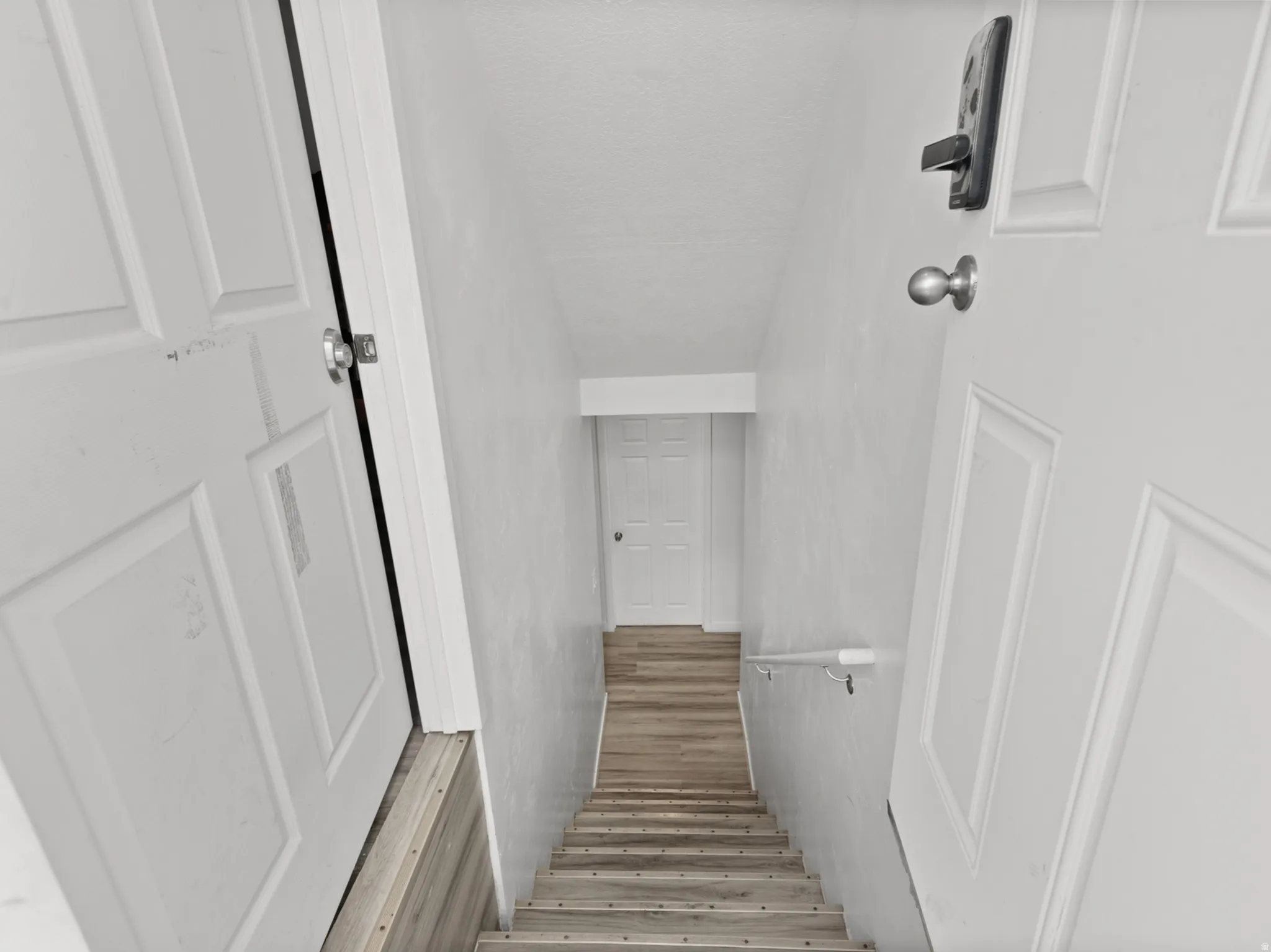 Staircase featuring wood-finish treads, a white handrail, and white walls