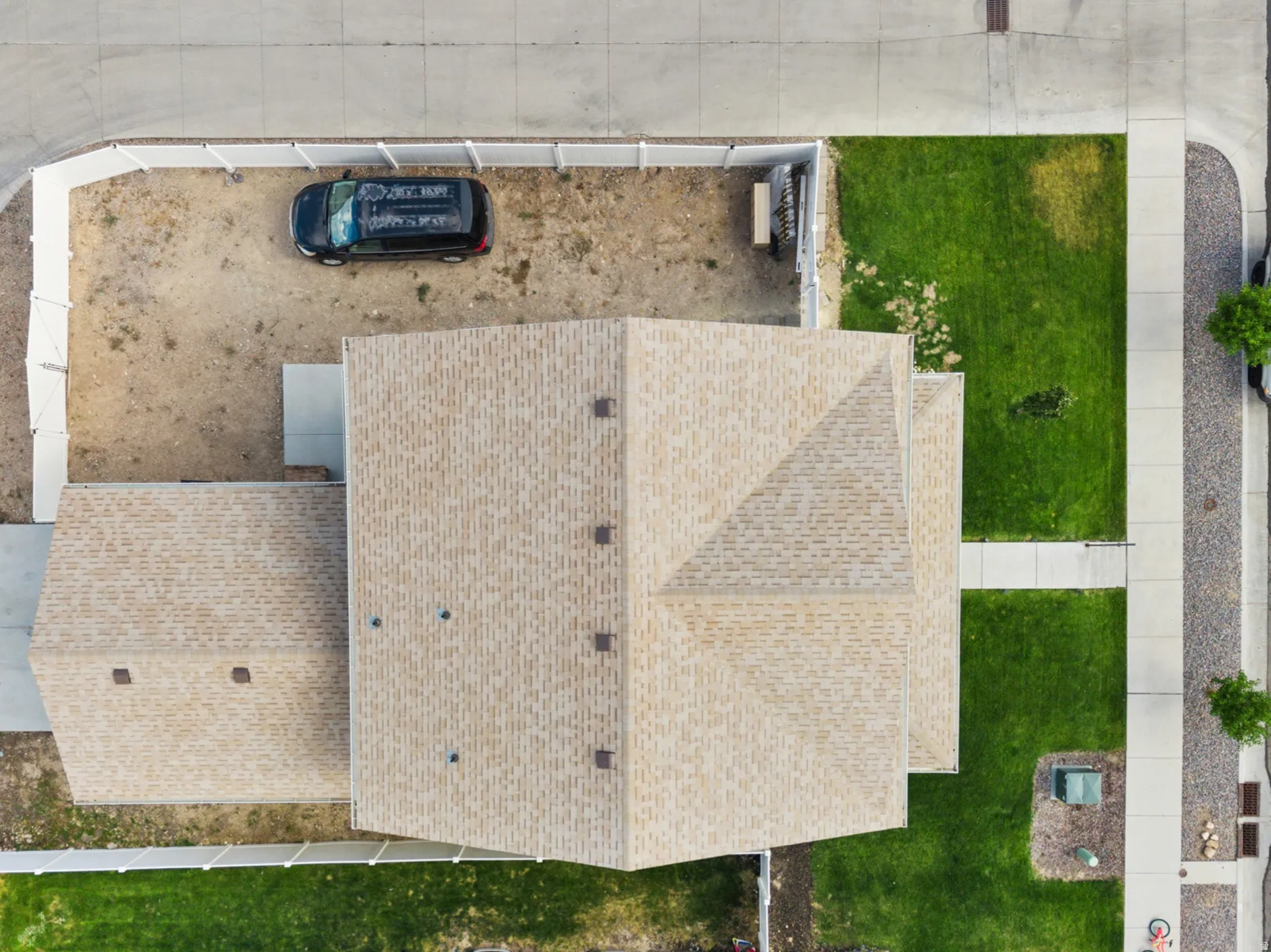 Aerial perspective highlighting the property with a light-colored shingle roof, concrete sidewalks, and a partially landscaped yard with grass sections and a gravel area