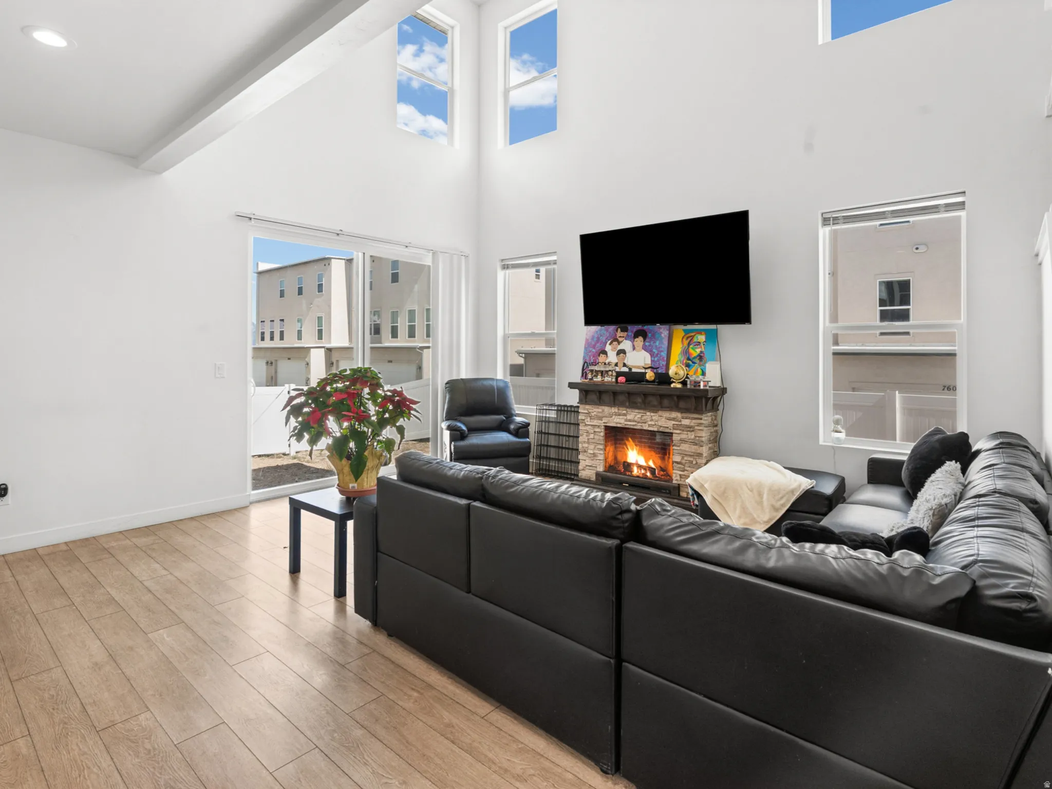 Vaulted ceiling living room featuring wood-finish flooring, a stone-faced fireplace with hearth, and a large sliding glass door