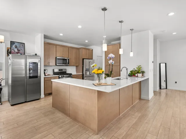 Open-concept kitchen featuring light wood-finish cabinetry, stainless steel appliances, and a central island with a white countertop