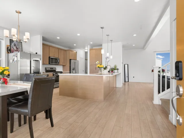 Open-concept kitchen and dining area featuring light wood-finish flooring, a kitchen island with pendant lighting, stainless steel appliances, and wood cabinetry