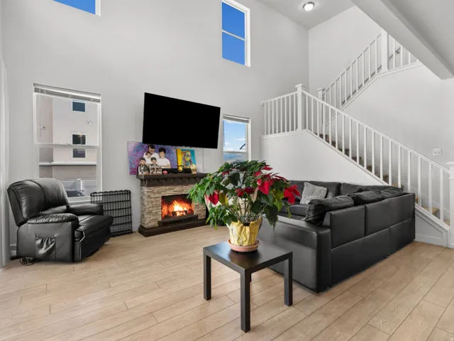 Living area featuring wood-finish flooring, a stone-front fireplace, and white walls
