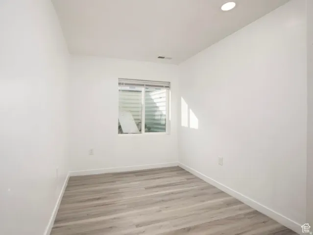 Room featuring light wood-finish flooring, white walls, and a window with blinds