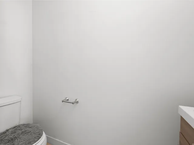White ceramic toilet, chrome toilet paper holder, and a vanity with wood-finish cabinetry