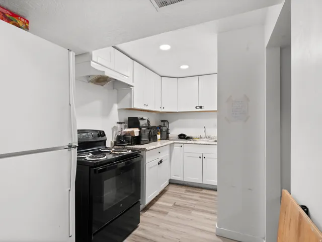 Kitchen featuring wood-finish flooring, white cabinetry with dark hardware, a white refrigerator, a black electric range, and recessed ceiling lighting
