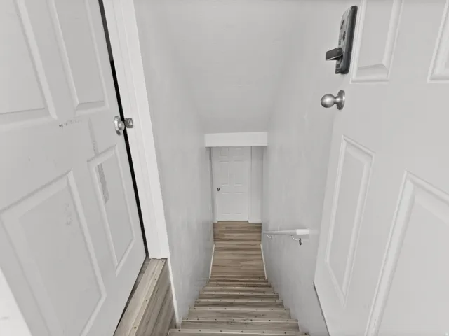 Staircase featuring wood-finish treads, a white handrail, and white walls