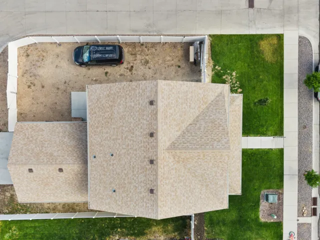 Aerial perspective highlighting the property with a light-colored shingle roof, concrete sidewalks, and a partially landscaped yard with grass sections and a gravel area
