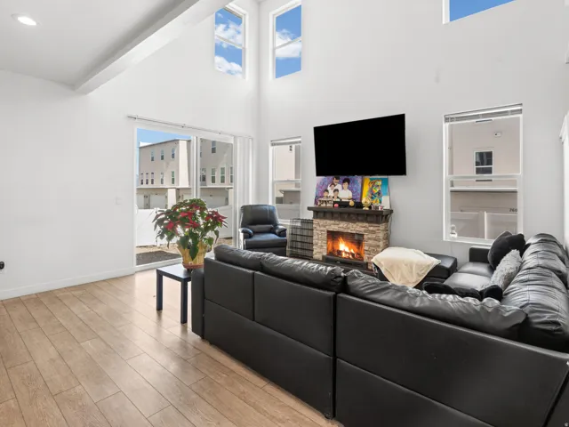 Vaulted ceiling living room featuring wood-finish flooring, a stone-faced fireplace with hearth, and a large sliding glass door