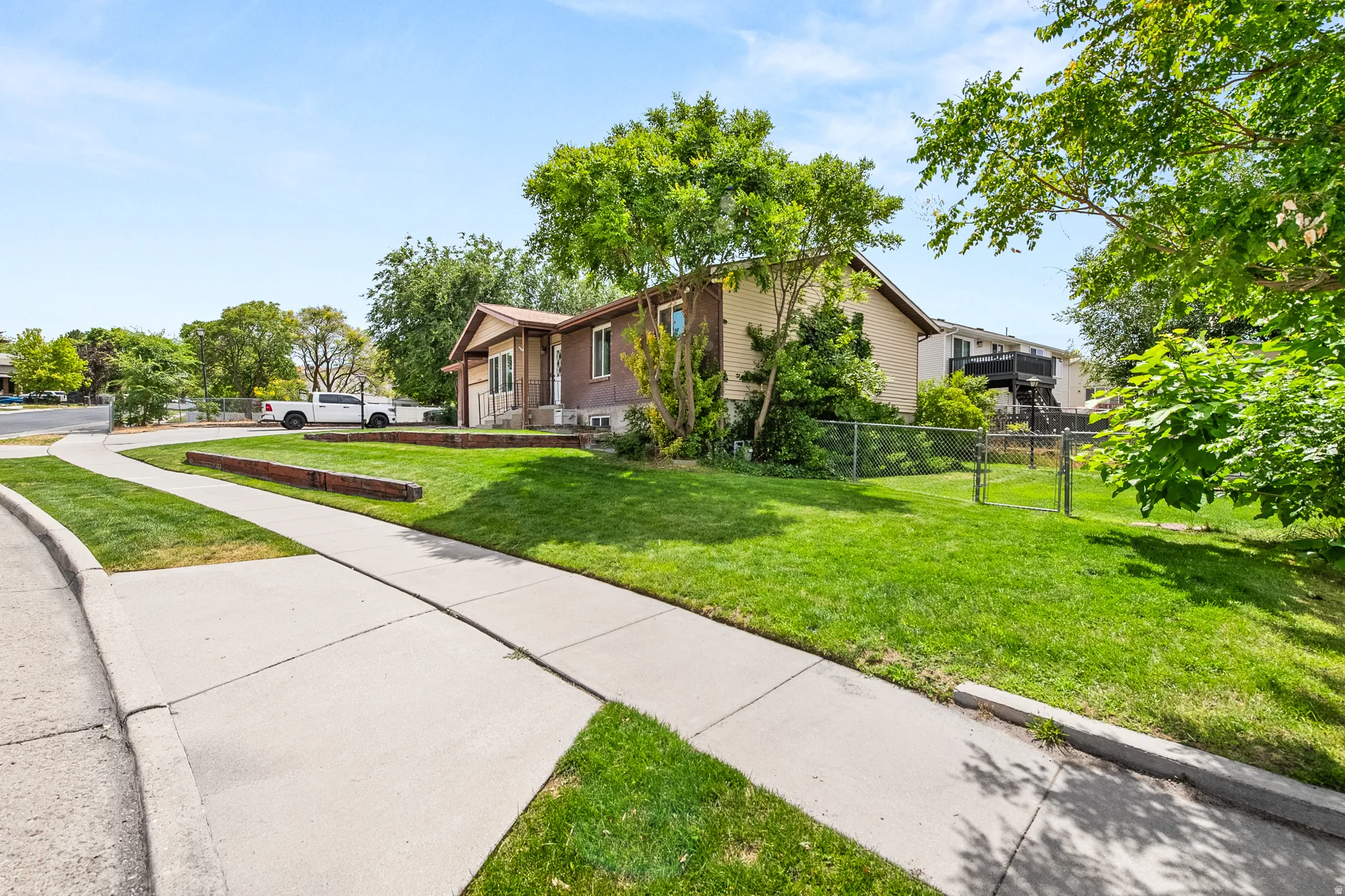 Expansive front yard featuring a manicured lawn, mature trees, and a concrete pathway
