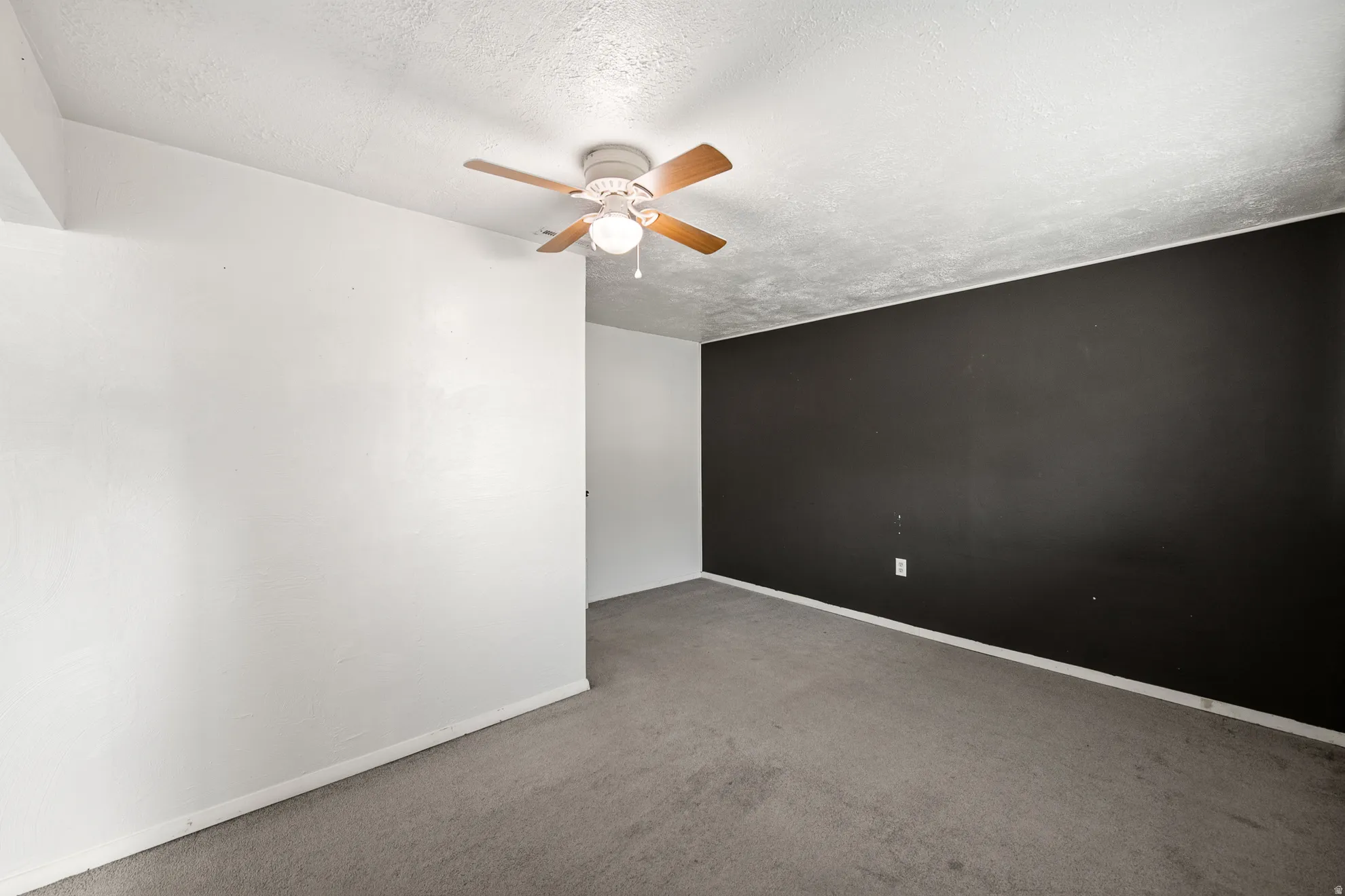 Room featuring a ceiling fan with light fixture, textured ceiling, carpet flooring, a dark accent wall, and white baseboards