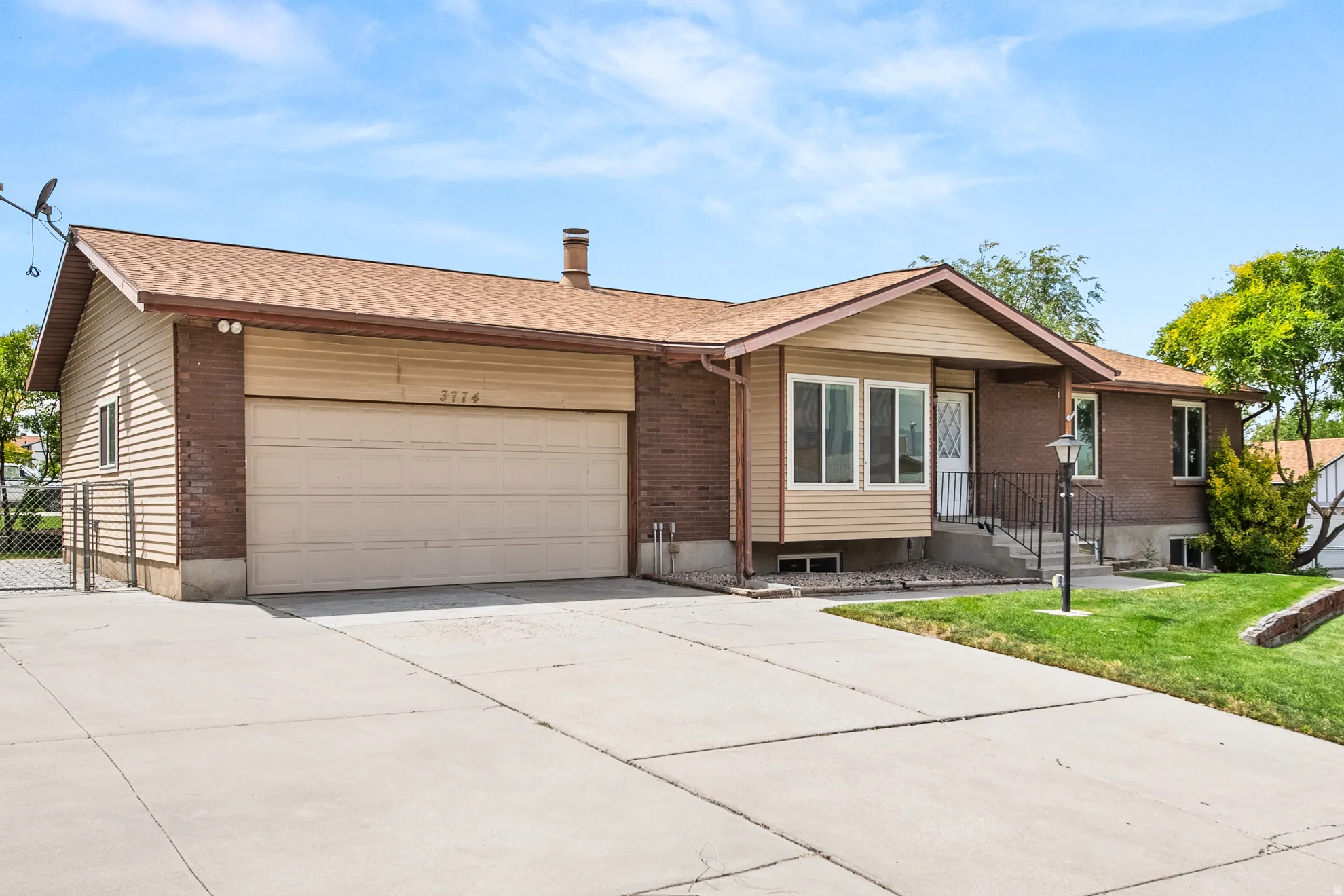 Brick and siding exterior featuring an attached garage with a concrete driveway, a front porch with railing, a front door with a decorative glass insert, and a landscaped lawn