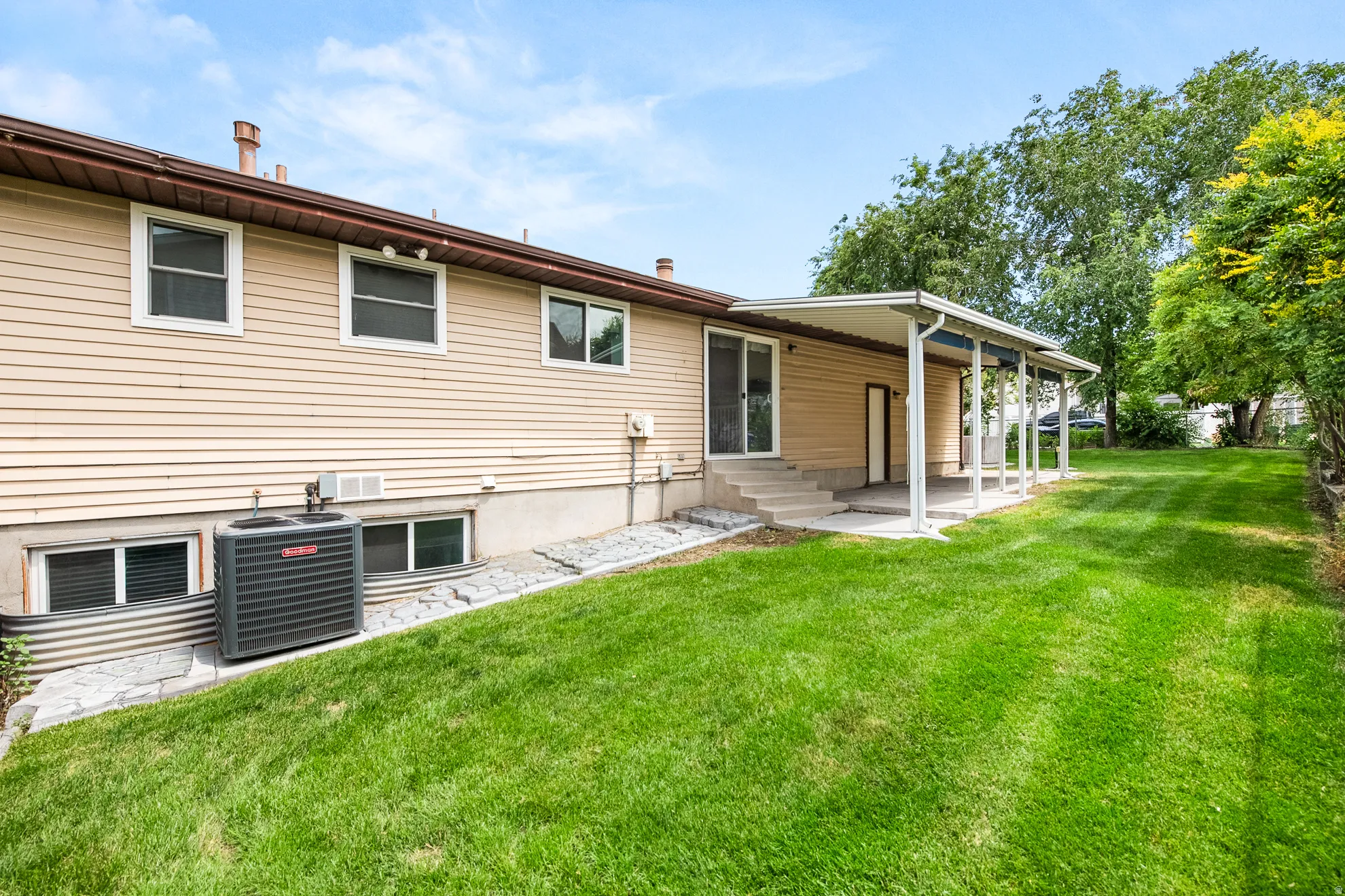 Expansive green lawn with a covered patio, multiple windows, and exterior siding