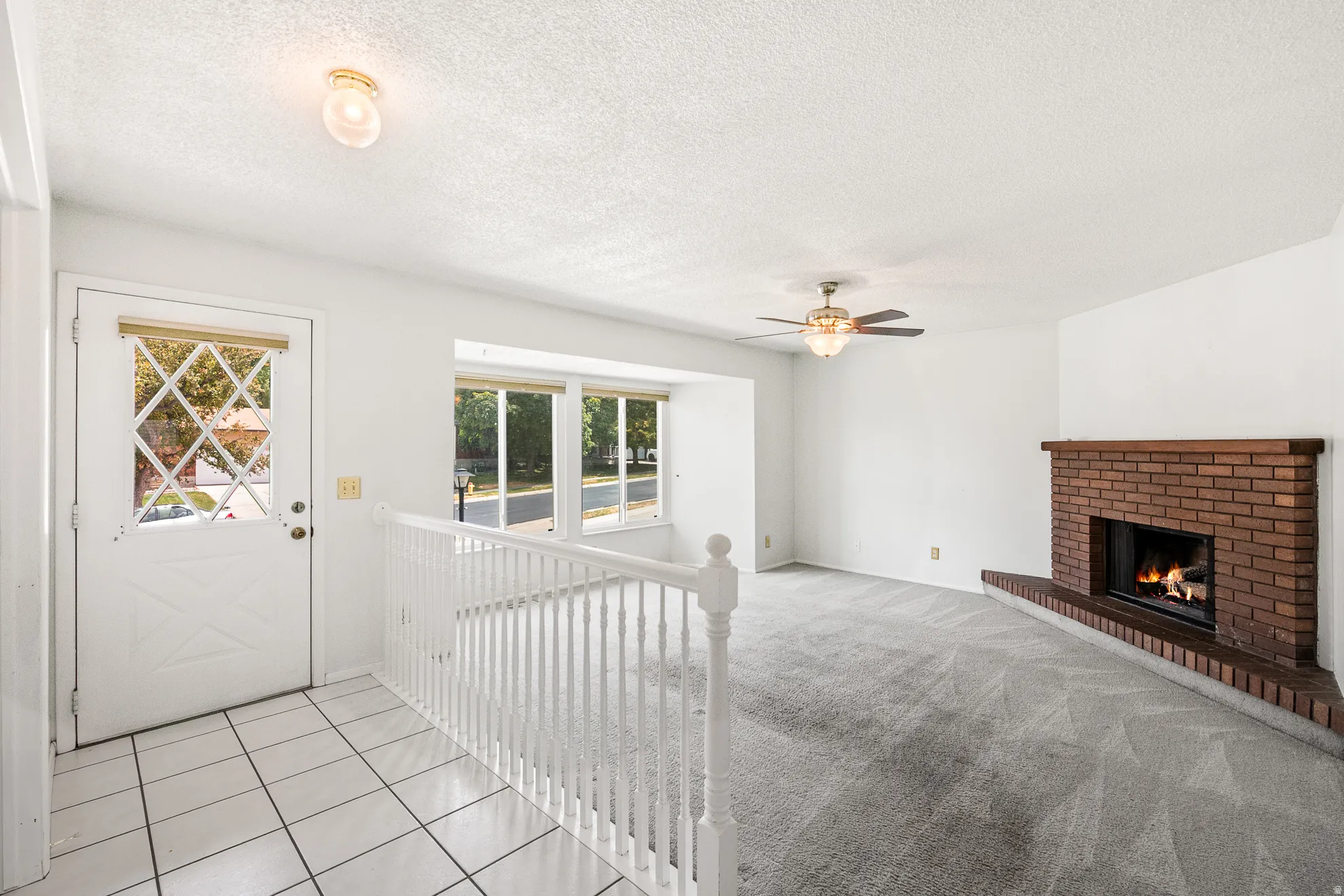 Inviting living area featuring a brick fireplace with a wood-finish mantel, neutral carpeting, and a ceiling fan