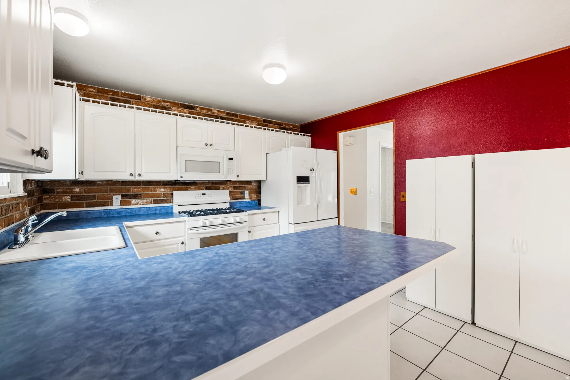 Kitchen featuring white cabinetry, blue countertops, brick-finish backsplash, and white appliances including a range and refrigerator