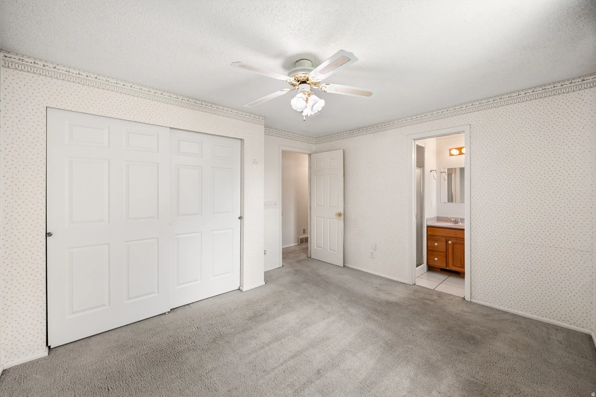 Carpeted room featuring a ceiling fan with integrated lighting, a large closet with sliding panel doors, and direct access to an en-suite bathroom with a vanity and mirror