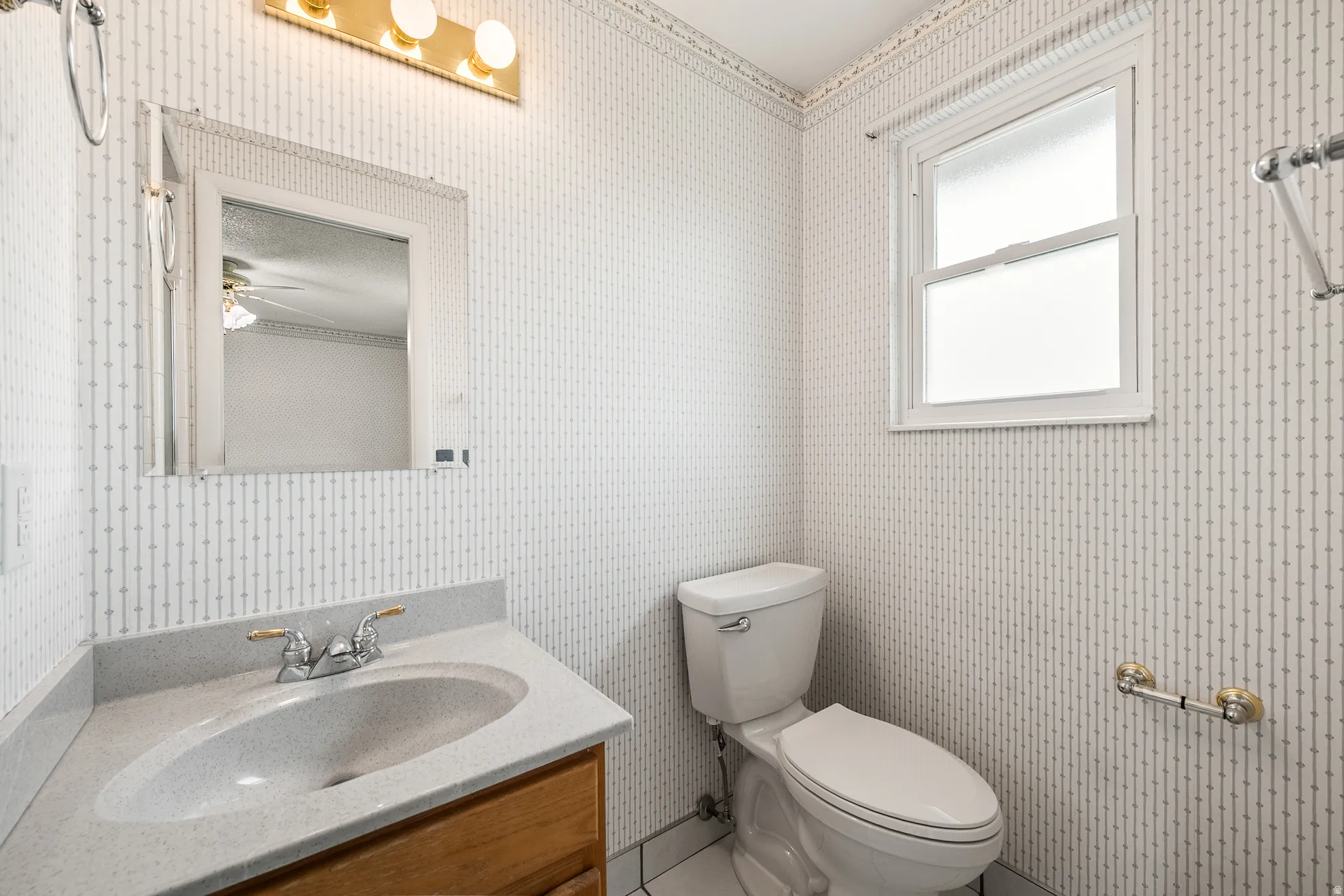 Bathroom featuring a corner vanity with integrated sink, a single window, a wall-mounted mirror, and a three-light fixture