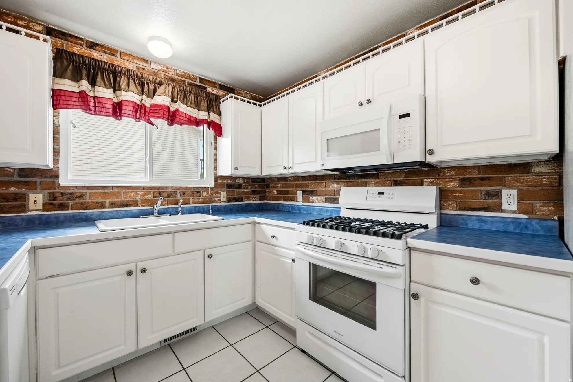 Kitchen featuring white cabinetry, blue countertops, brick-style backsplash, white appliances, and tiled flooring