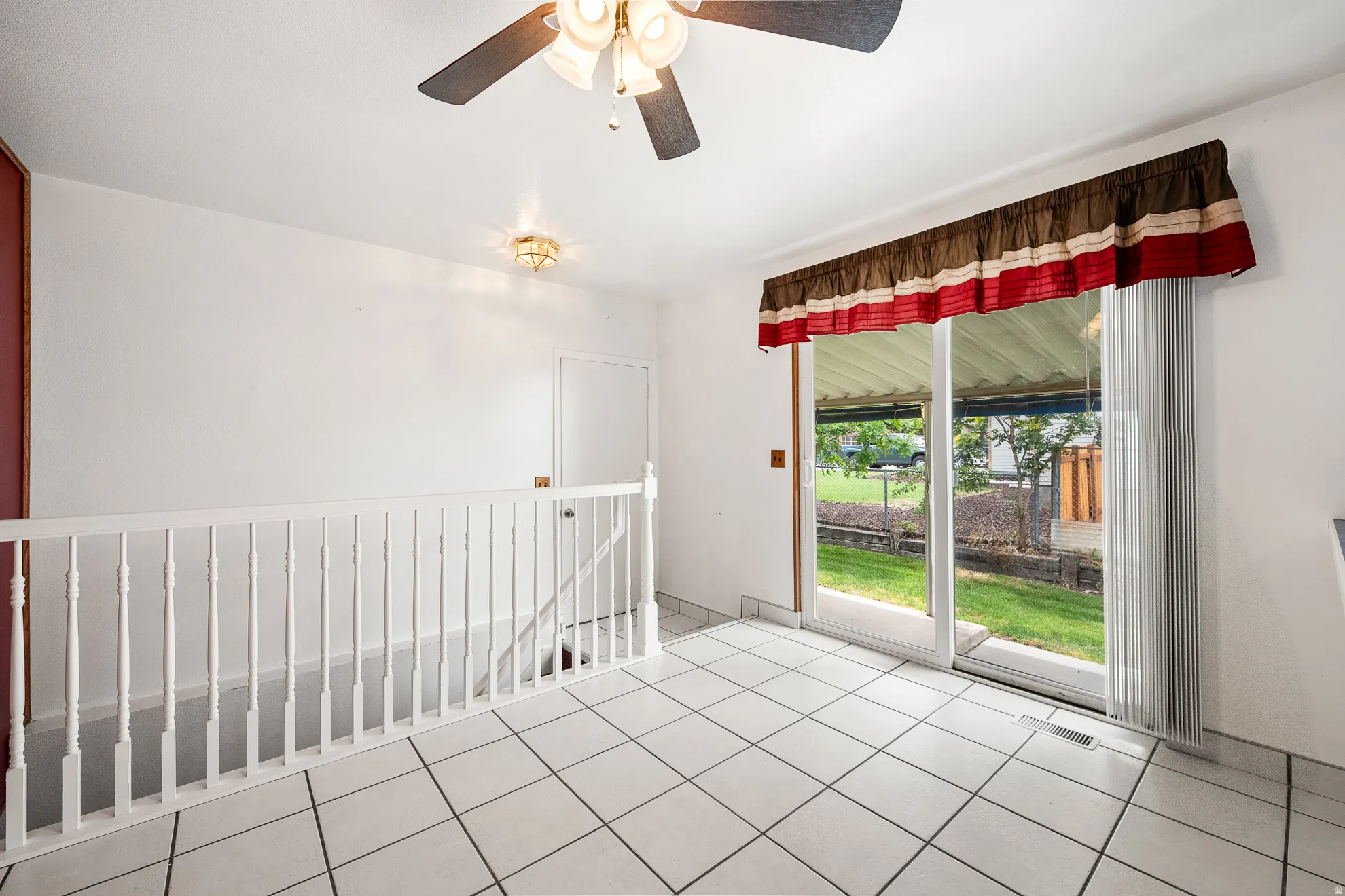 Spacious room featuring white tile flooring, white railing, and a sliding glass door leading to the exterior