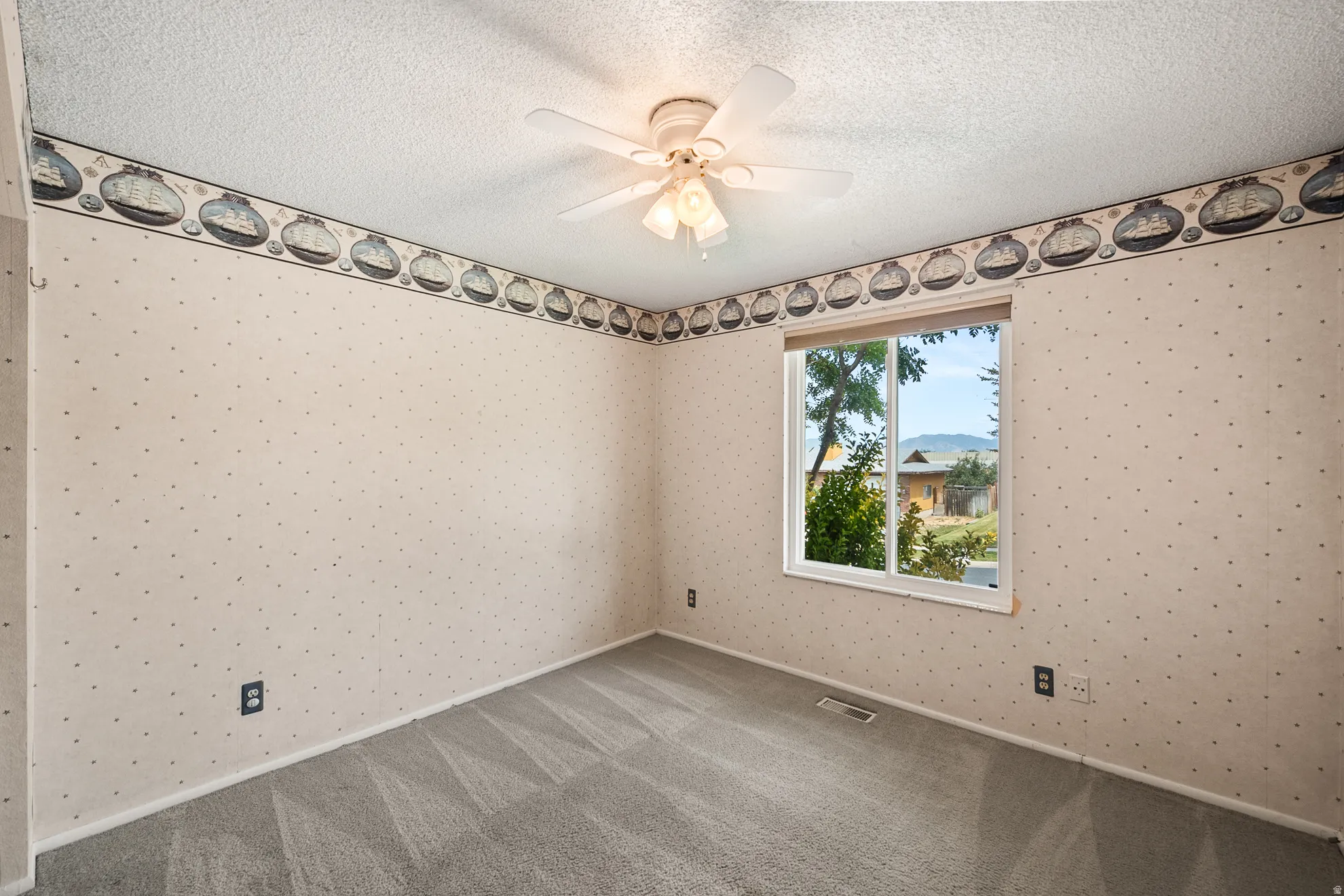 Room featuring textured walls with a patterned border, gray carpeting, and a white ceiling fan with integrated lighting