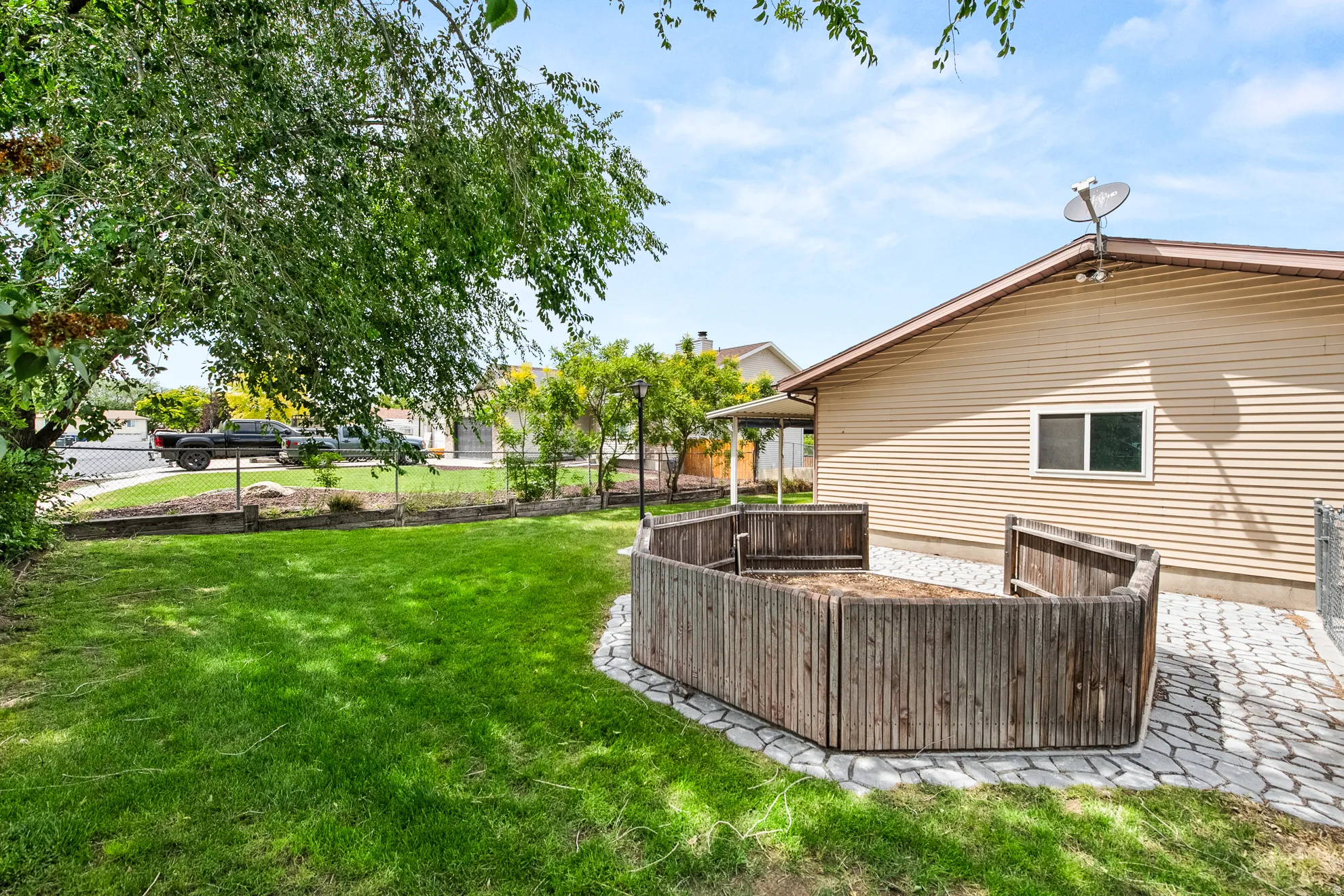 Expansive green lawn with mature shade tree, a paver patio, and a built-in wooden planter box