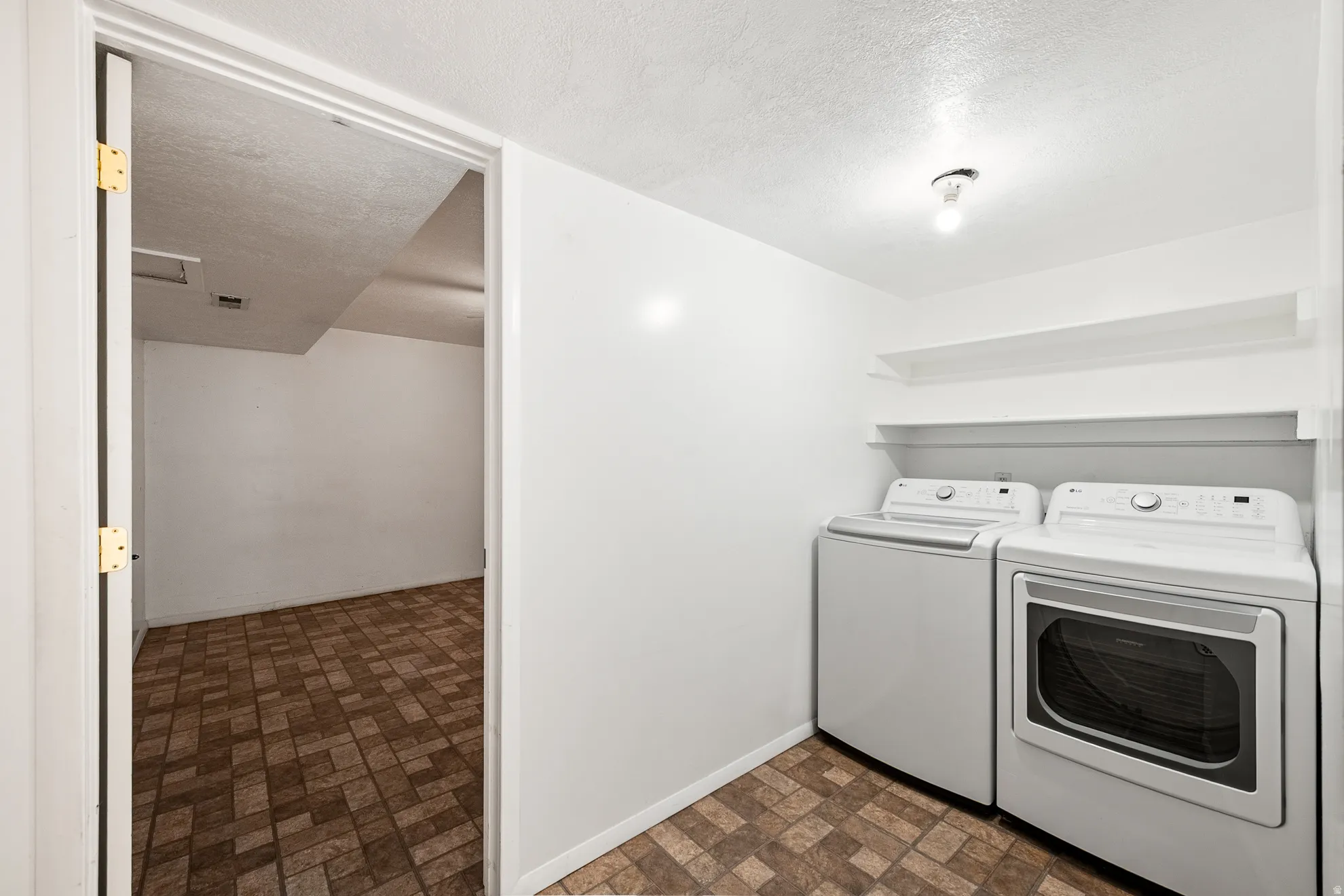 Laundry area featuring a top-load washing machine, front-load dryer, and two wall-mounted shelves
