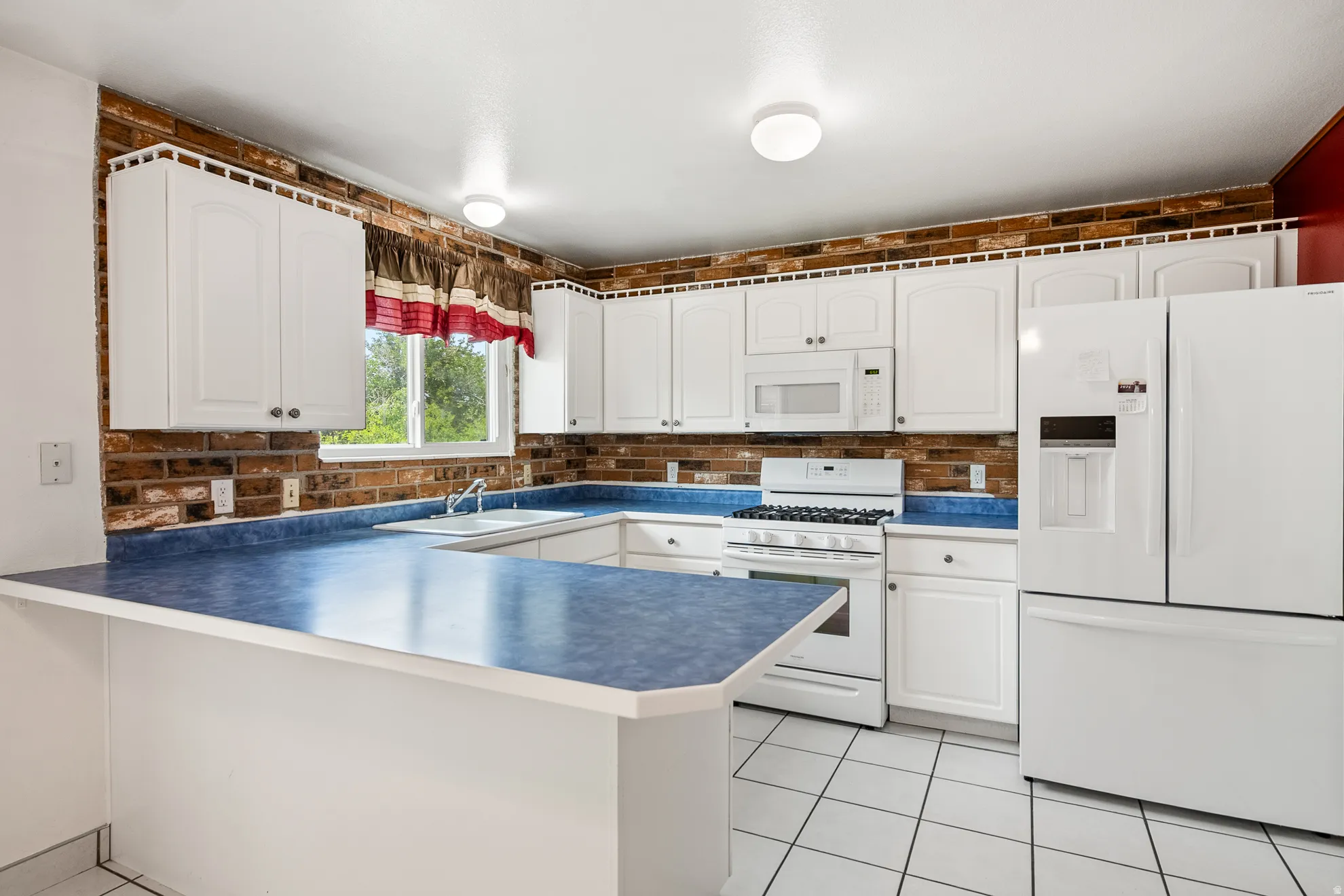 Kitchen featuring white cabinetry, brick-finish backsplash, blue countertops, and white appliances