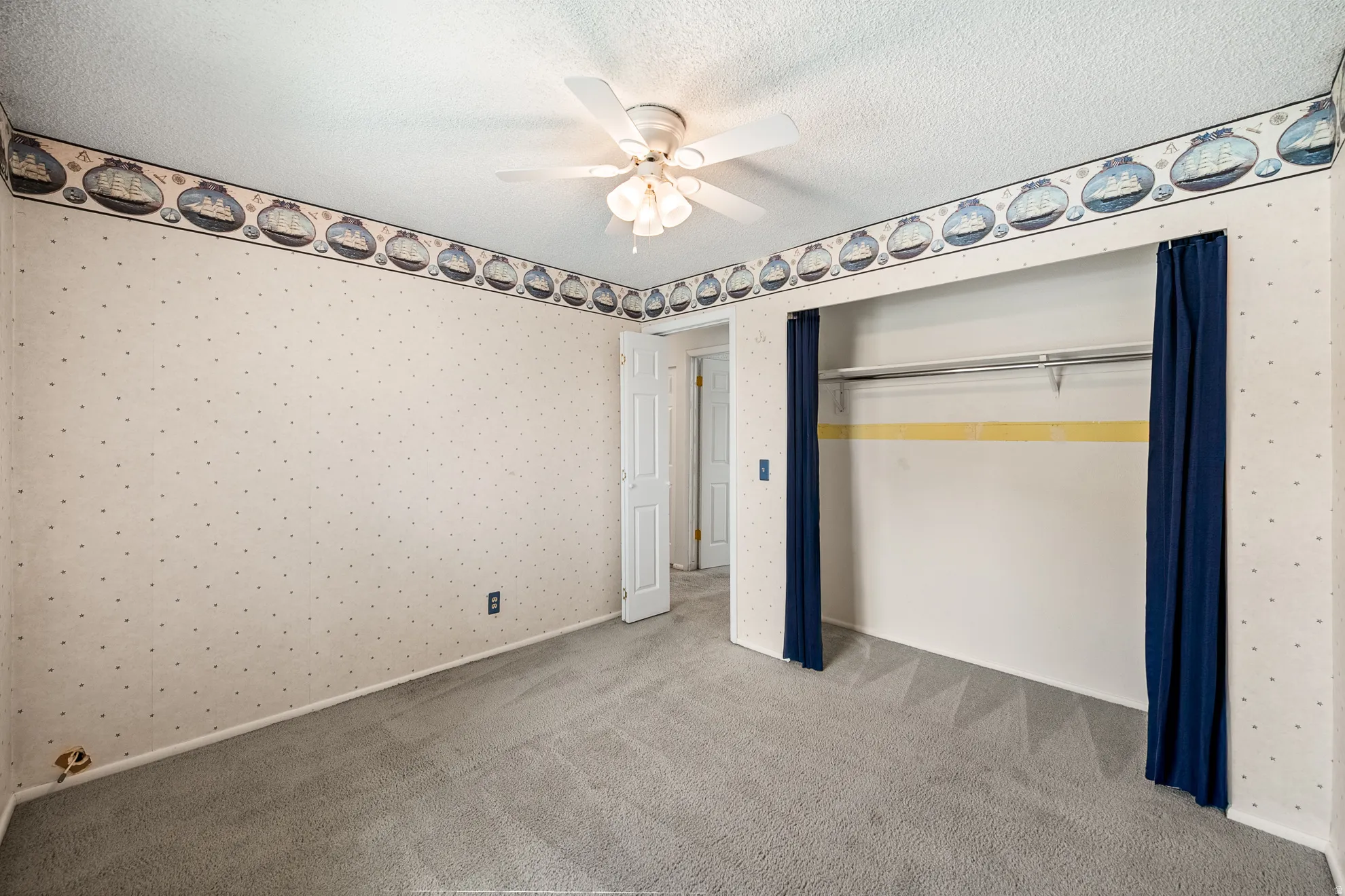 Carpeted room featuring a ceiling fan with integrated lighting, a built-in closet with hanging rod and shelf, and a painted trim baseboard