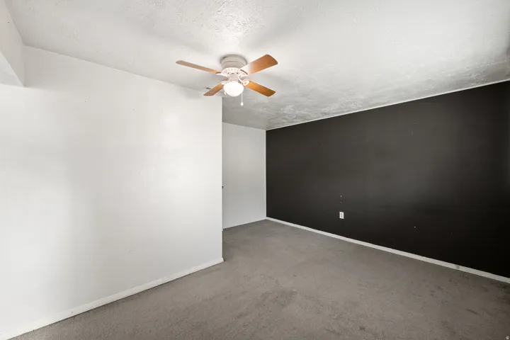 Room featuring a ceiling fan with light fixture, textured ceiling, carpet flooring, a dark accent wall, and white baseboards