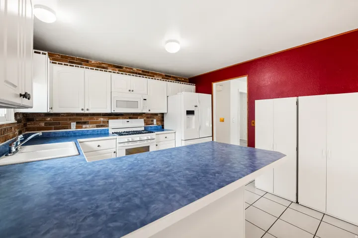 Kitchen featuring white cabinetry, blue countertops, brick-finish backsplash, and white appliances including a range and refrigerator