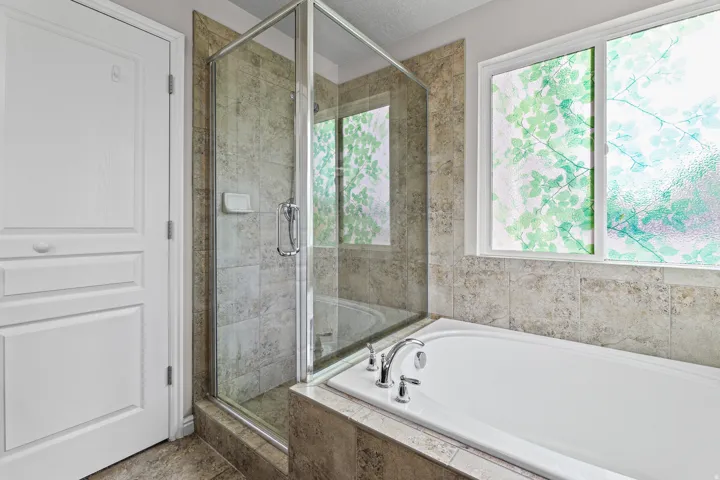 Spa-inspired primary bath featuring a soaking tub and separate glass-enclosed shower, complemented by large windows that provide abundant natural light.